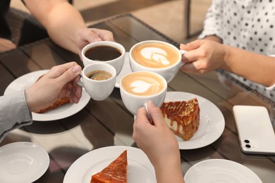 Photo of Friends drinking coffee at wooden table in outdoor cafe, closeup