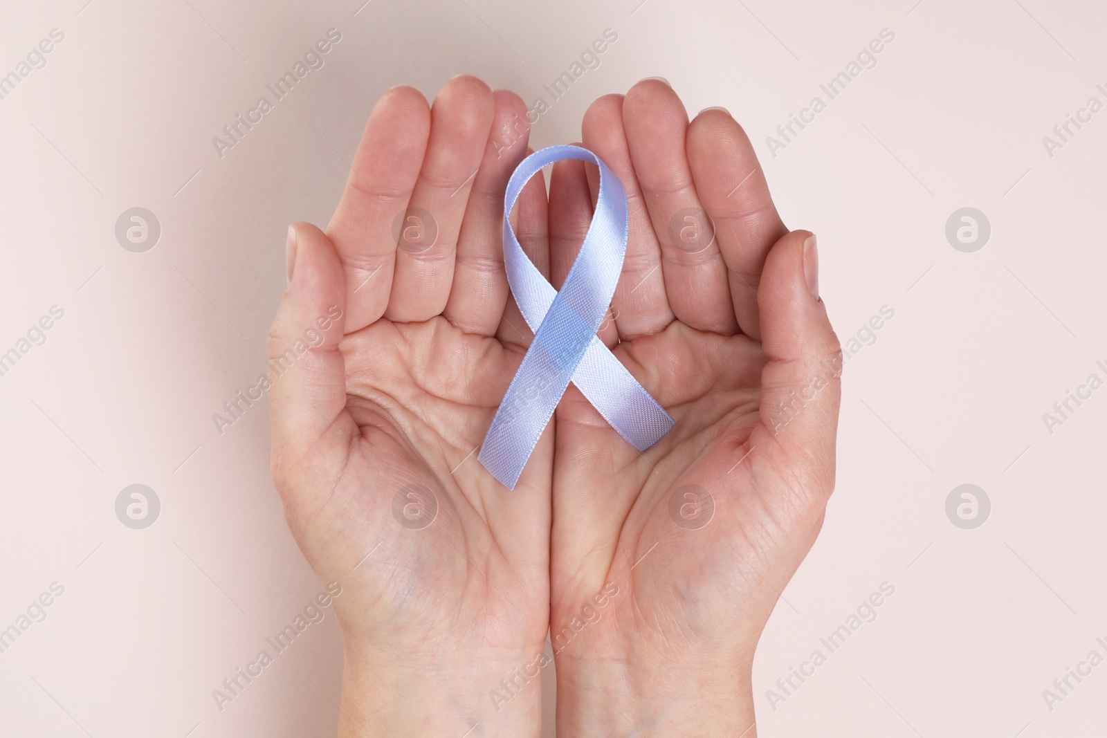 Photo of International Psoriasis Day. Woman with light blue ribbon as symbol of support on beige background, top view