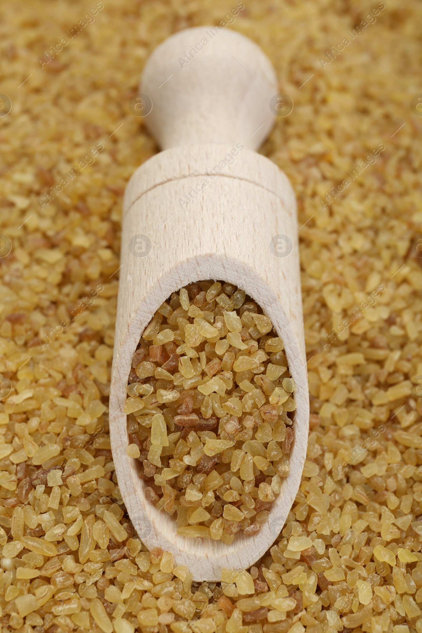 Photo of Wooden scoop on pile of uncooked bulgur, closeup view