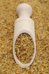 Photo of Wooden scoop on pile of uncooked bulgur, closeup view