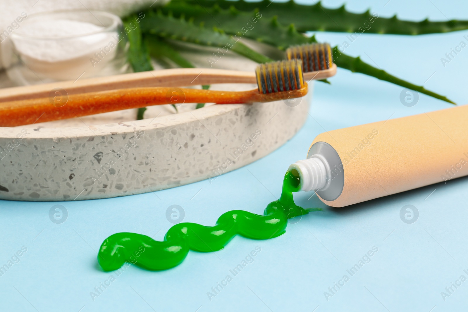 Photo of Tube of toothpaste, toothbrushes and fresh aloe on light blue background, closeup