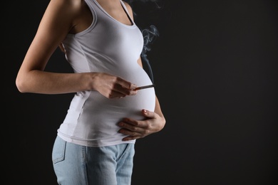 Photo of Pregnant woman smoking cigarette on black background, closeup. Space for text