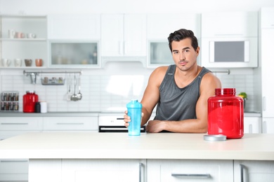 Photo of Young athletic man with protein shake powder in kitchen, space for text
