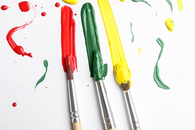 Photo of Brushes with different paints and strokes on white background, flat lay