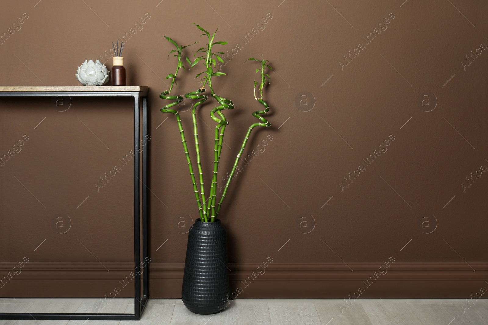 Photo of Vase with green bamboo stems on floor near brown wall indoors, space for text. Interior design