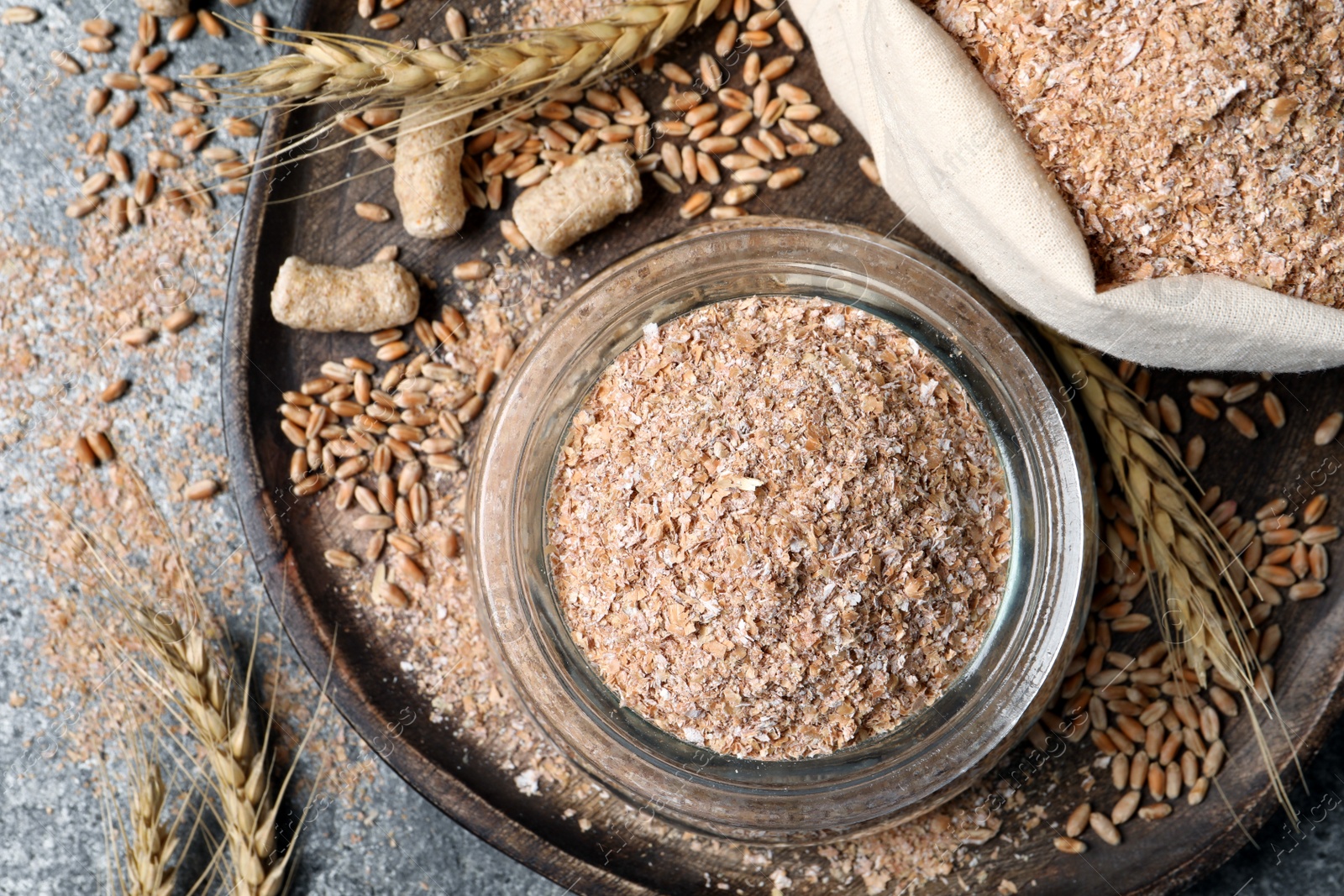 Photo of Jar and sack with wheat bran on grey table, flat lay