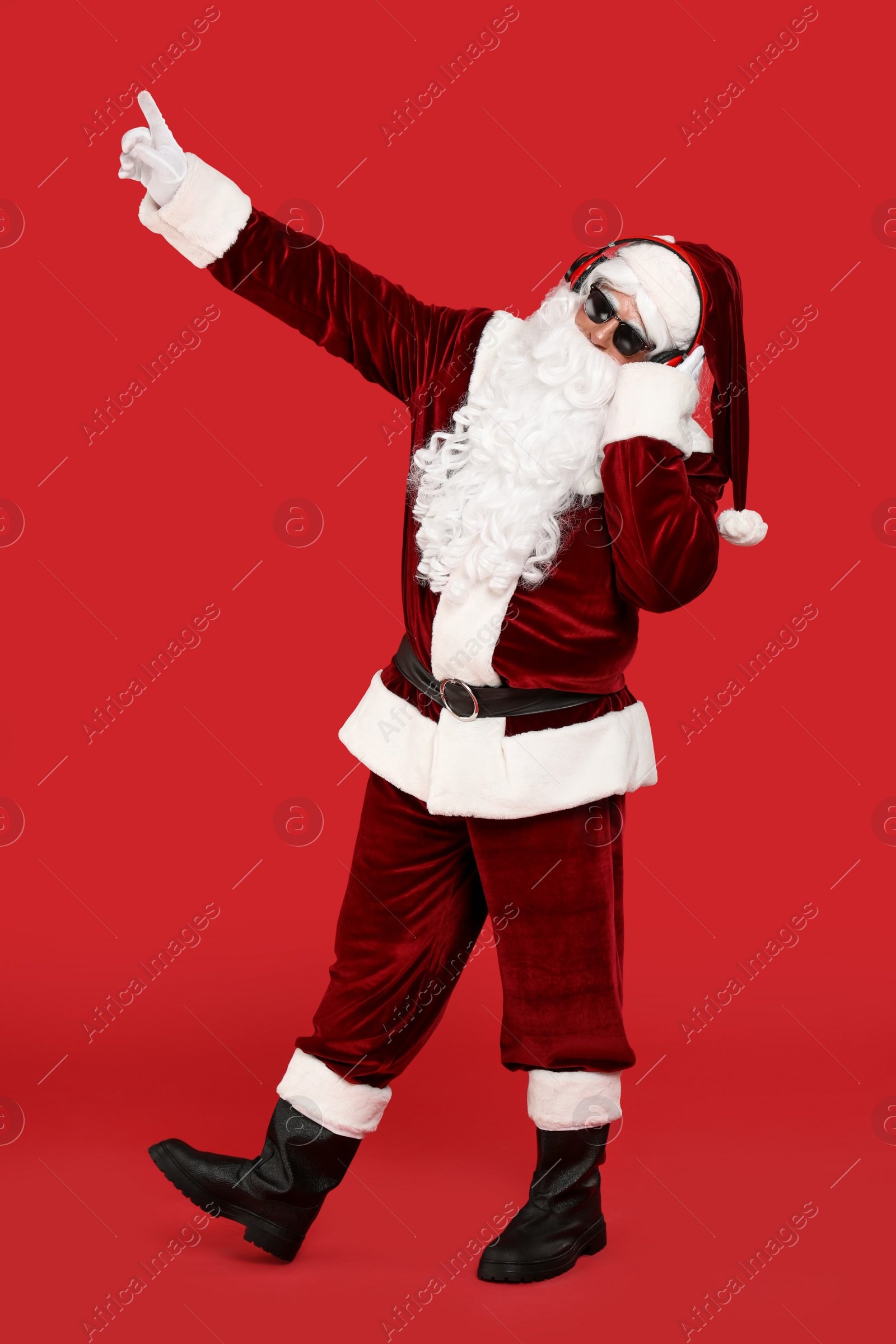 Photo of Santa Claus with headphones listening to Christmas music on red background