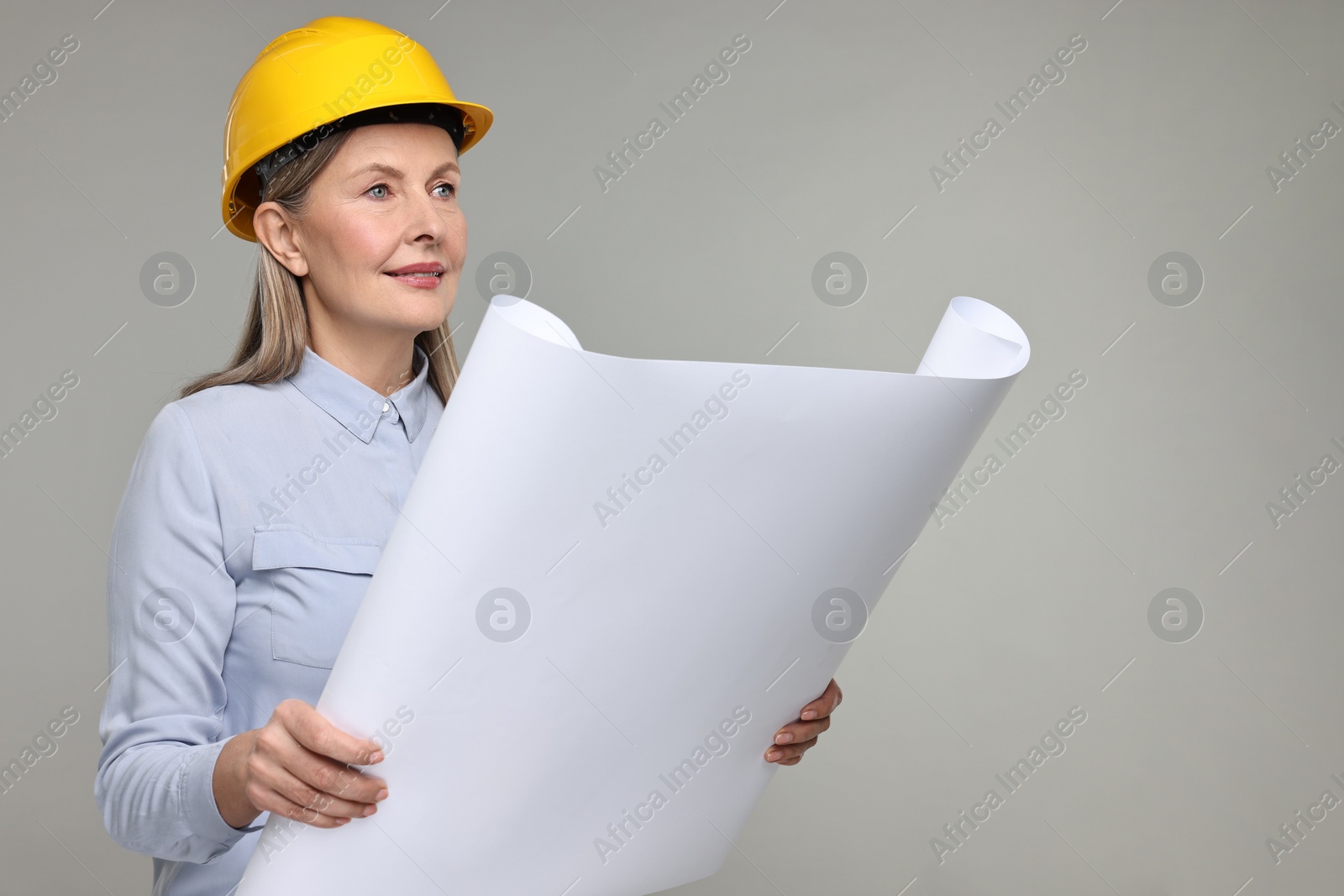 Photo of Architect in hard hat with draft on grey background