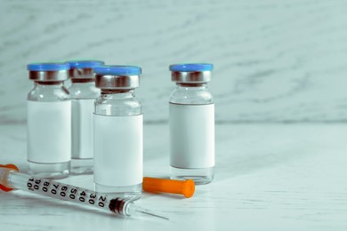 Medication in glass vials and syringe on white wooden table, space for text