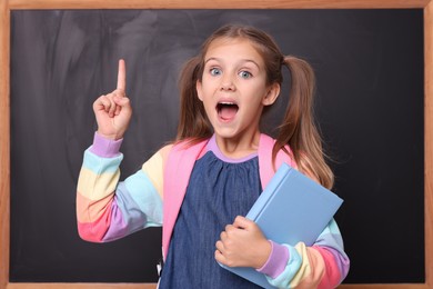Excited schoolgirl with book pointing at something near blackboard