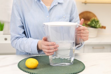 Photo of Woman with water filter jug and lemon at white marble table in kitchen, closeup