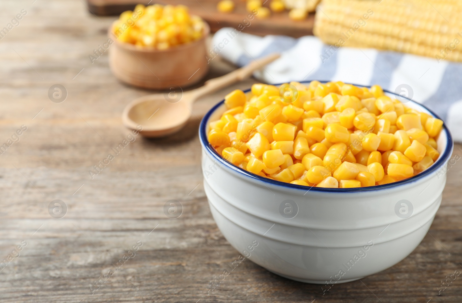 Photo of Delicious canned corn in bowl on wooden table, closeup. Space for text