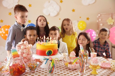 Photo of Cute children blowing out candles on birthday cake at table indoors