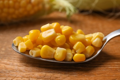 Photo of Spoon of preserved corn on wooden table, closeup