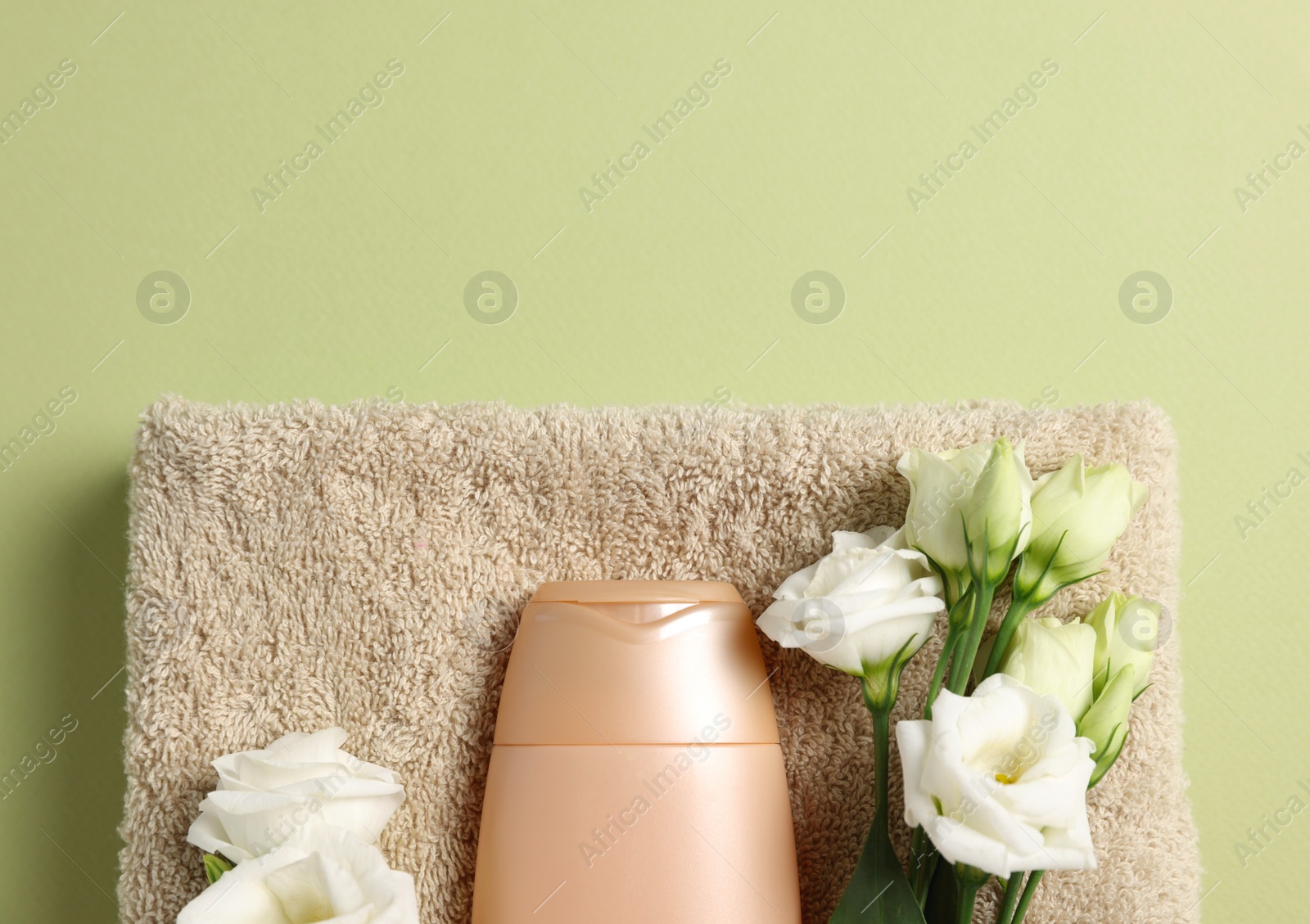 Photo of Soft folded towel with flowers and cosmetic product on green background, top view. Space for text
