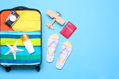 Photo of Open suitcase and beach objects on blue background, flat lay. Space for text
