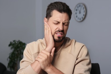 Photo of Man suffering from ear pain on in room