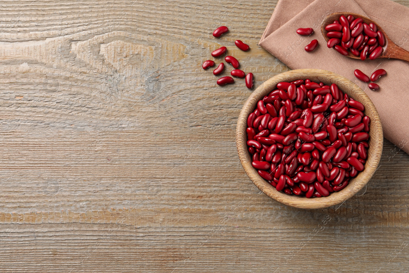 Photo of Raw red kidney beans with bowl, spoon and napkin on wooden table, flat lay. Space for text