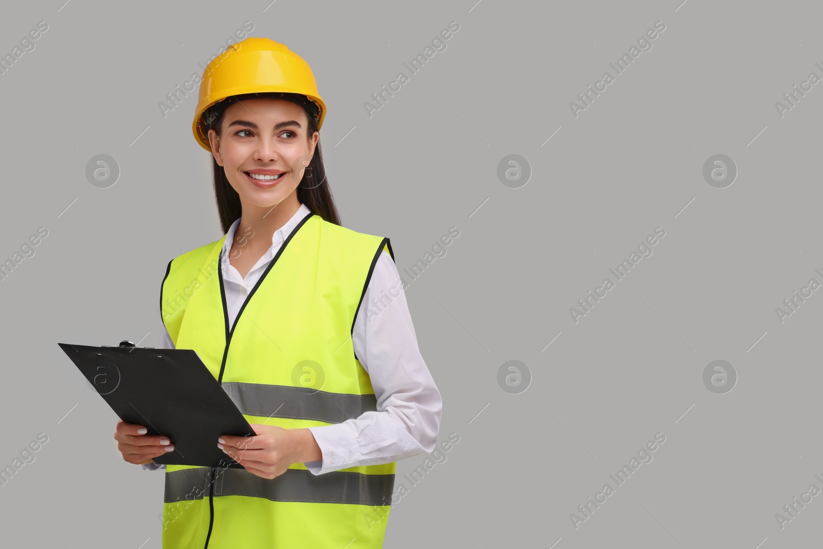 Photo of Engineer in hard hat holding clipboard on grey background, space for text