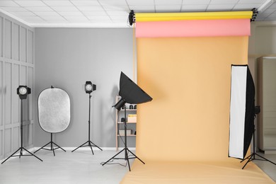 Photo of Pale orange photo background and professional lighting equipment in modern studio