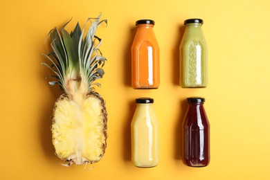 Photo of Bottles with delicious colorful juices and cut pineapple on yellow background, flat lay