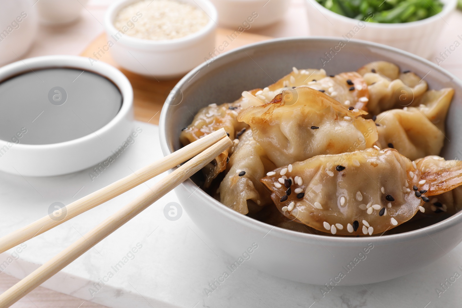 Photo of Delicious gyoza (asian dumplings) with sesame, soy sauce and chopsticks on table, closeup