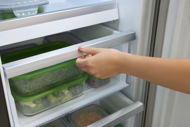 Photo of Woman pulling out fridge drawer with different fresh products, closeup. Food storage