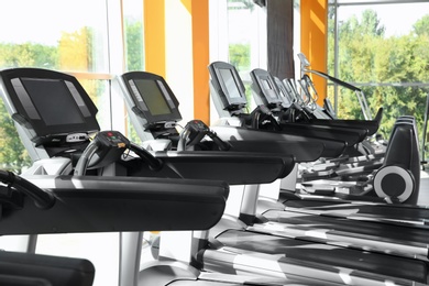 Photo of Gym interior with row of treadmills near windows
