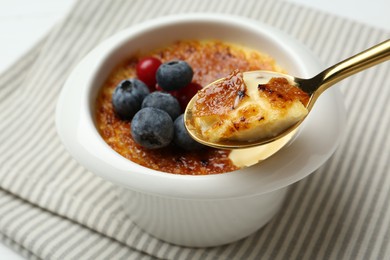 Photo of Eating delicious creme brulee with berries from spoon at white table, closeup