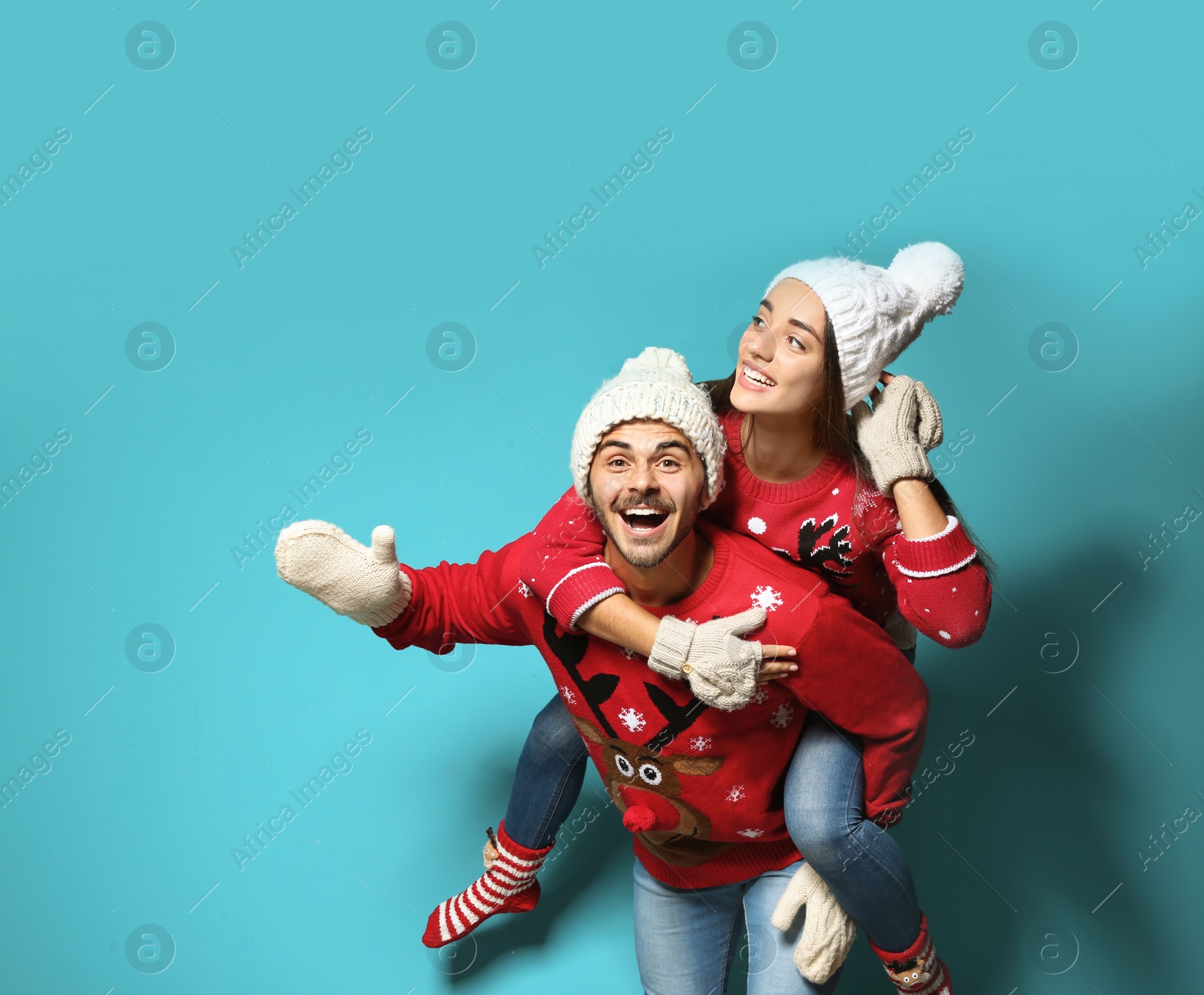 Photo of Young couple in Christmas sweaters and knitted hats on color background