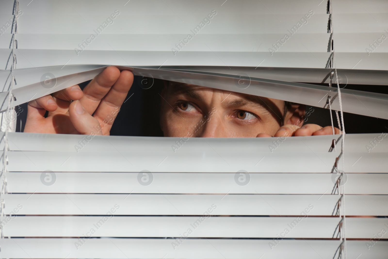 Photo of Curious man looking through Venetian window blinds