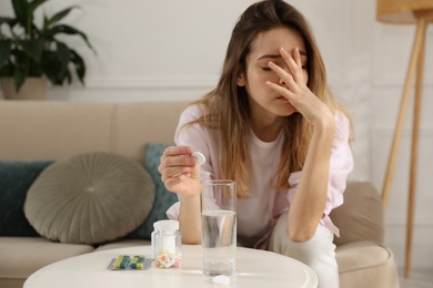Photo of Woman putting medicine for hangover into glass of water at home