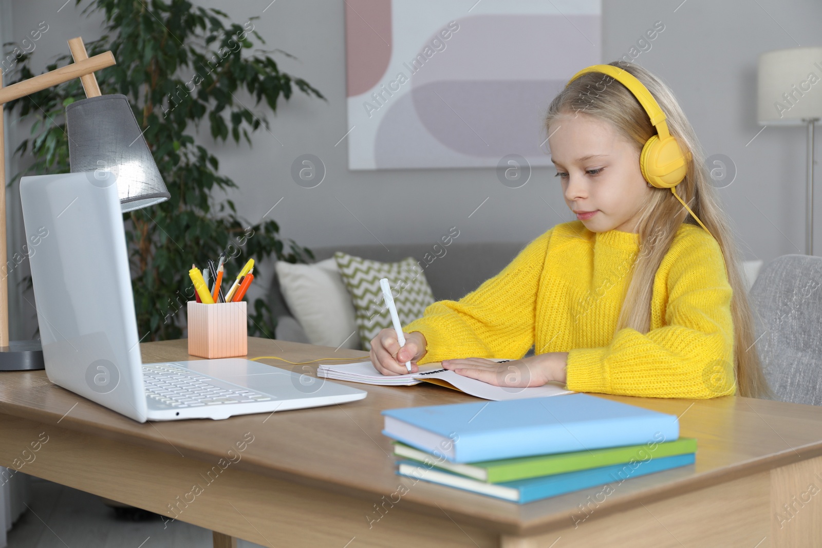 Photo of Cute little girl with modern laptop studying online at home. E-learning