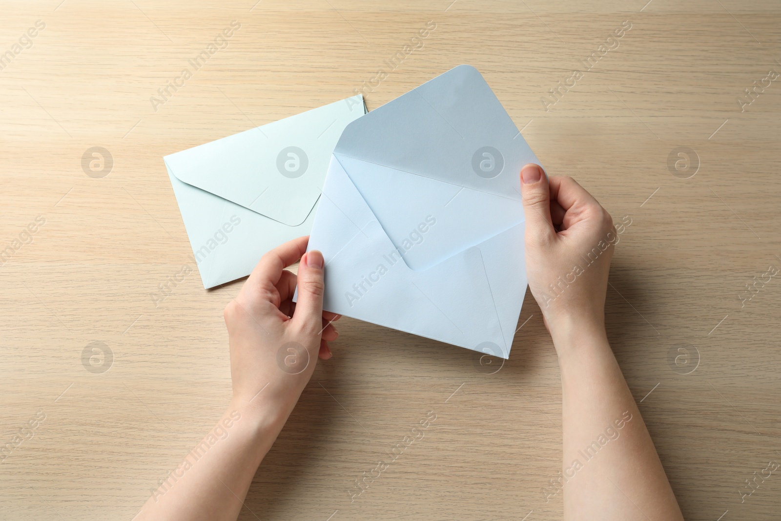 Photo of Woman with white paper envelopes at wooden table, top view