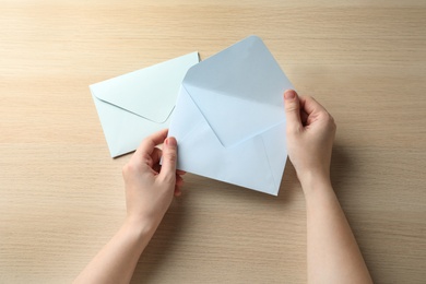 Woman with white paper envelopes at wooden table, top view