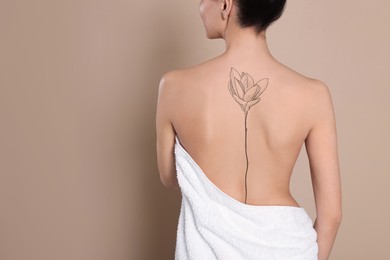 Young woman with tattoo of beautiful magnolia flower on beige background, back view. Space for text