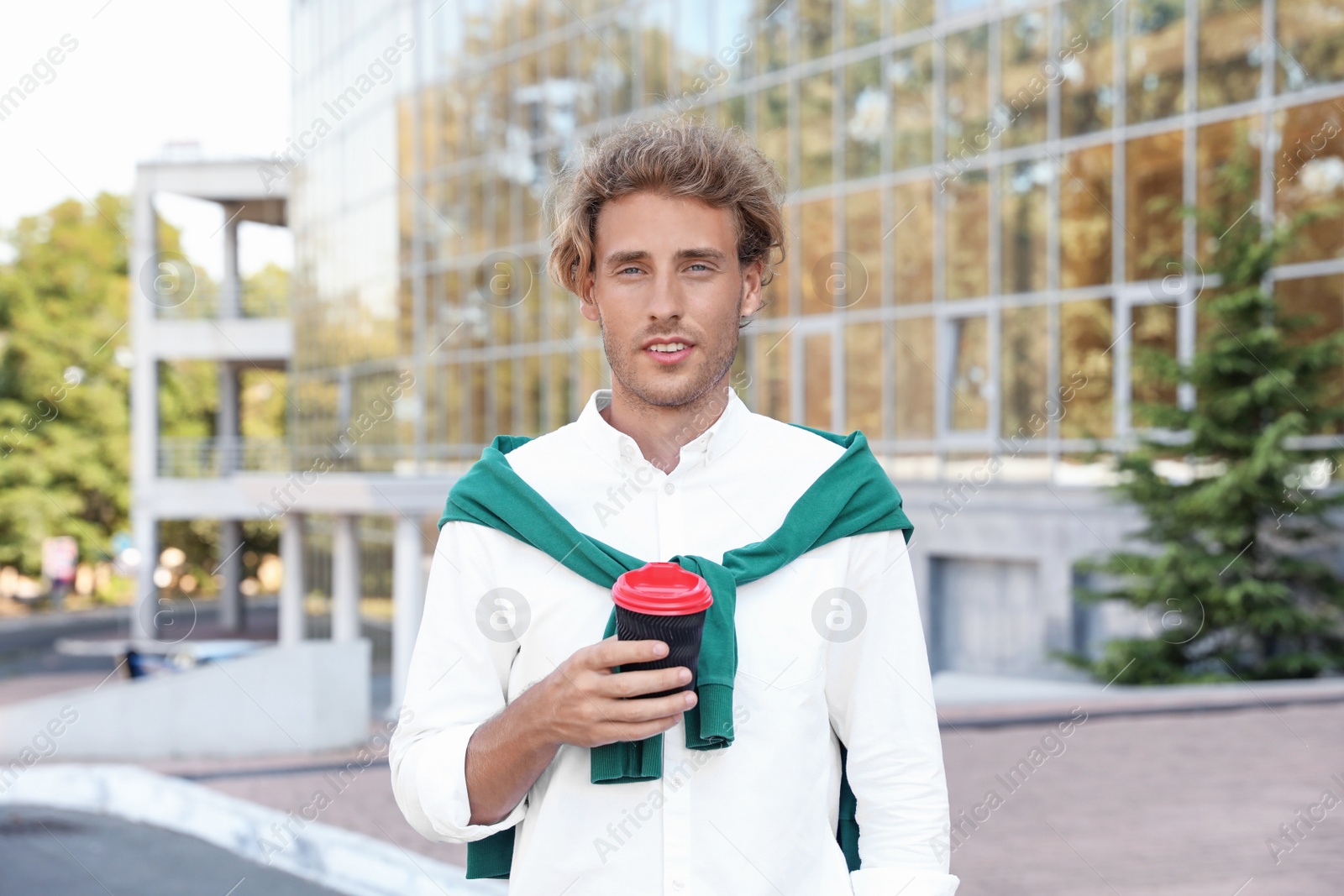 Photo of Portrait of handsome young man with cup of coffee on city street