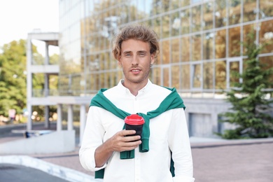 Portrait of handsome young man with cup of coffee on city street