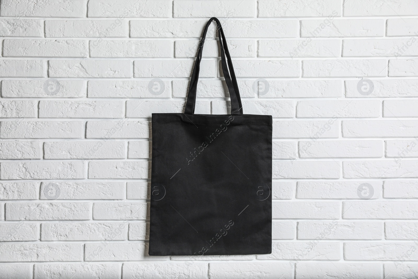 Photo of Eco tote bag hanging on white brick wall. Space for design