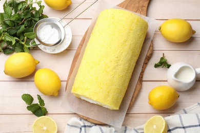 Photo of Delicious cake roll, lemons, mint and powdered sugar on light wooden table, flat lay
