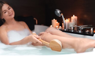 Photo of Beautiful woman rubbing leg with while taking bubble bath, focus on brush. Romantic atmosphere