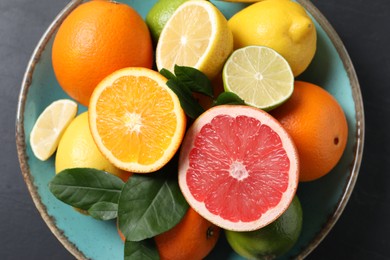 Photo of Different cut and whole citrus fruits on black table, top view