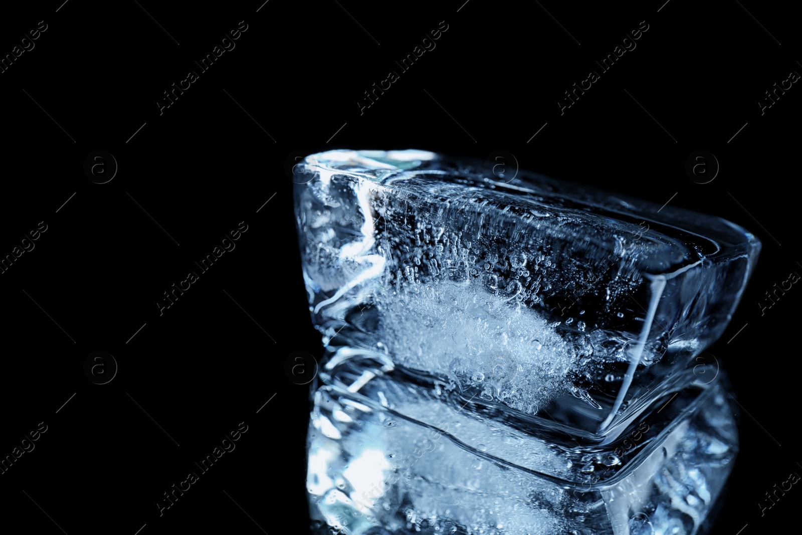 Photo of Ice cube on black mirror surface. Space for text