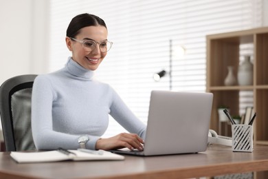 Young woman in glasses watching webinar at table in office