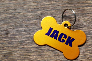 Image of Yellow metal pet tag in shape of bone on wooden table, closeup. Space for text