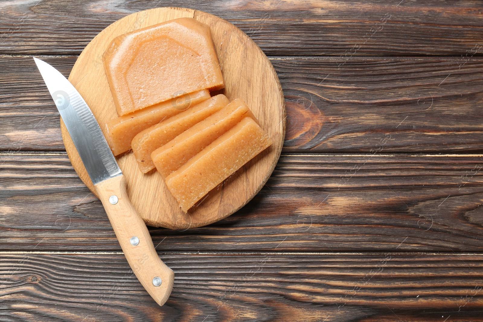 Photo of Tasty sweet quince paste and knife on wooden table, top view. Space for text