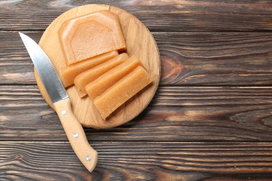 Tasty sweet quince paste and knife on wooden table, top view. Space for text