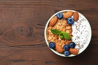 Photo of Healthy homemade granola with yogurt on wooden table, top view. Space for text
