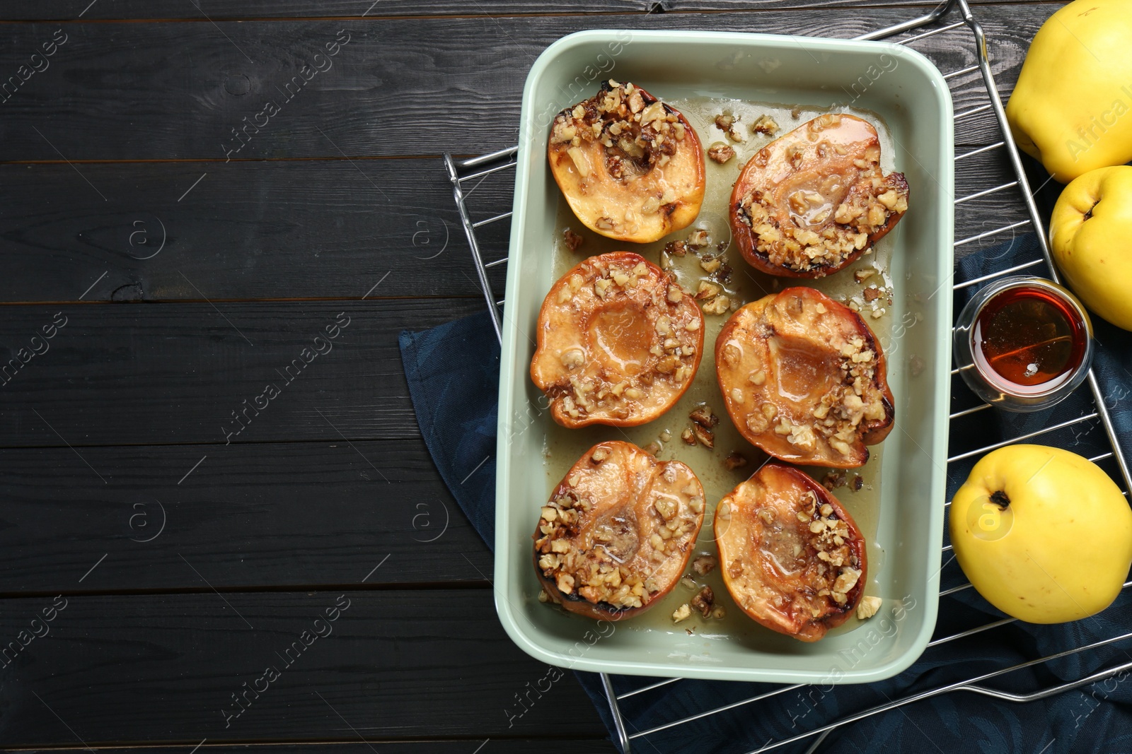 Photo of Tasty baked quinces with nuts and honey in dish on black wooden table, flat lay. Space for text