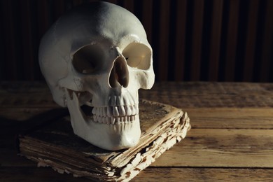 Photo of Human skull and old book on wooden table, space for text